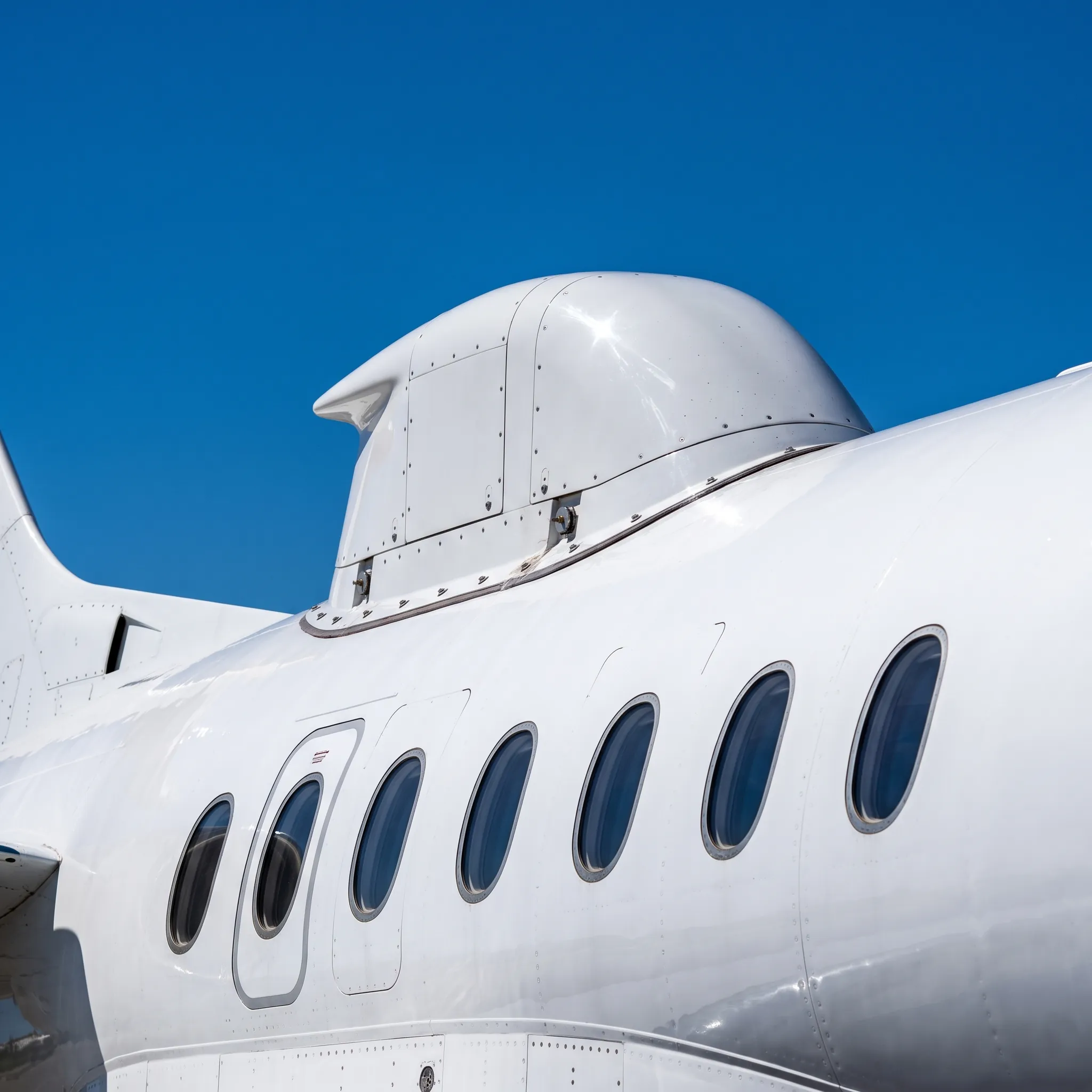 Close-up of a satellite antenna fairing on top of a private jet fuselage against a clear blue sky