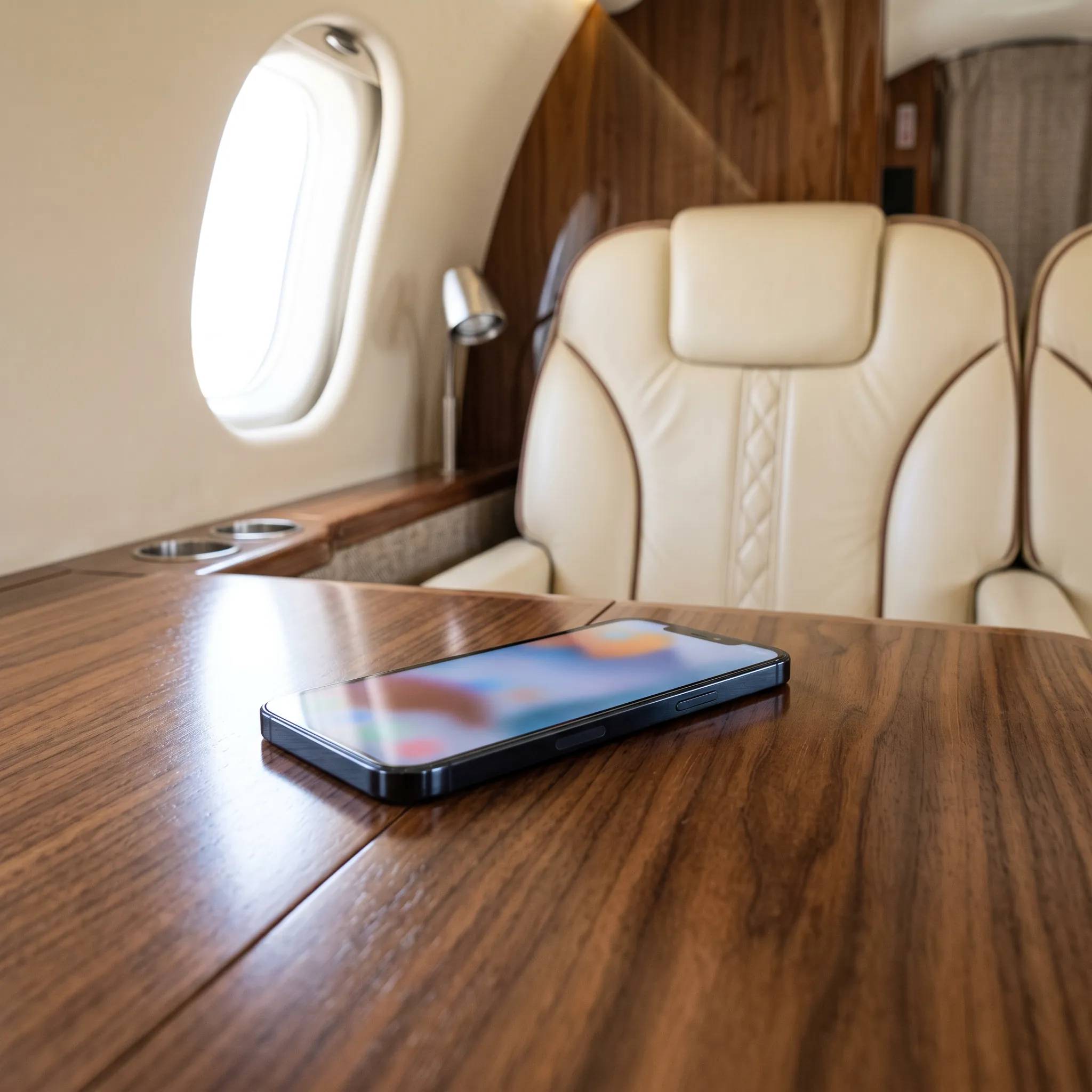Smartphone on a walnut table inside a private jet cabin with cream leather seats